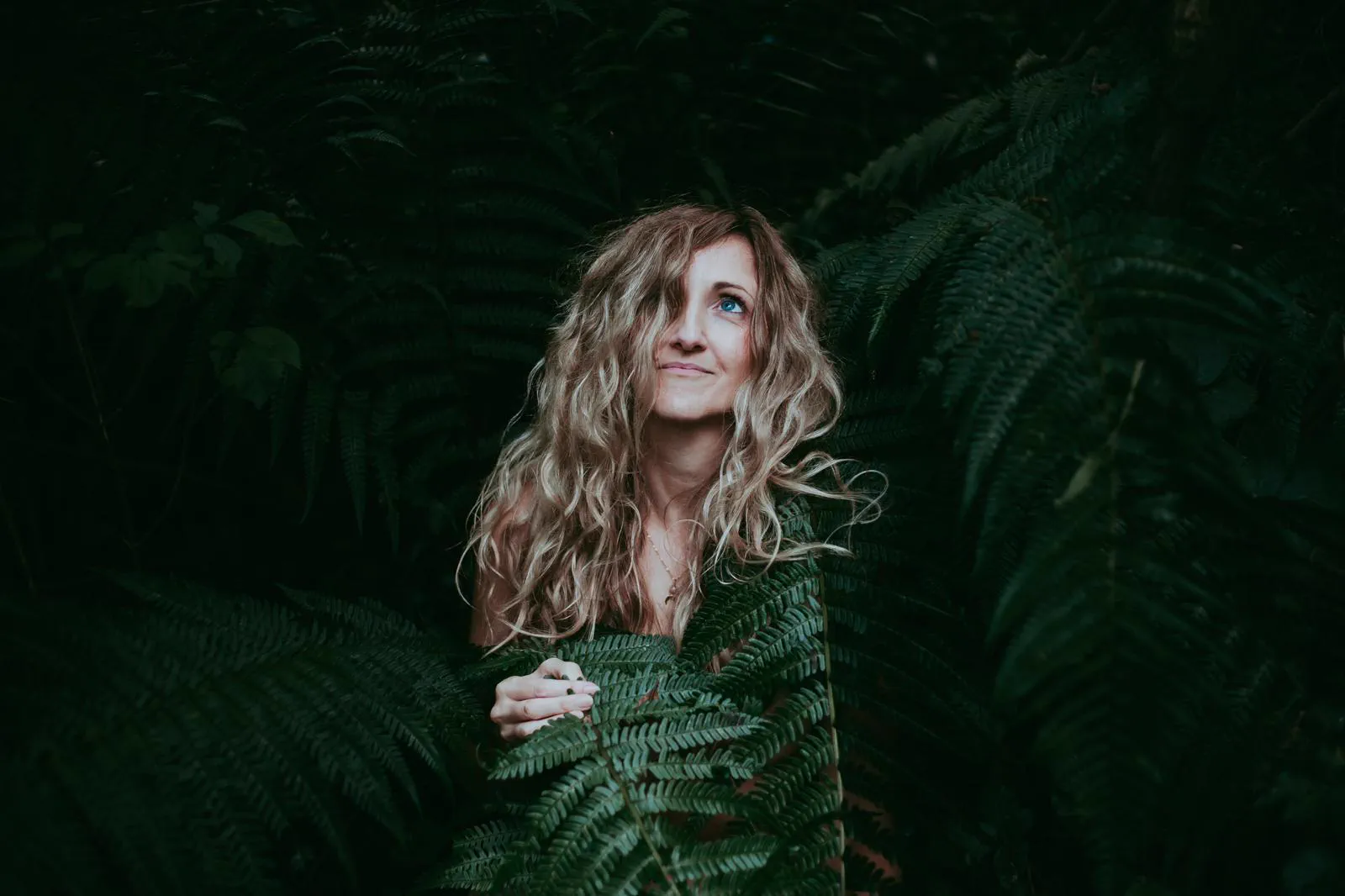 Samantha looking up softly, surrounded by fern fronds